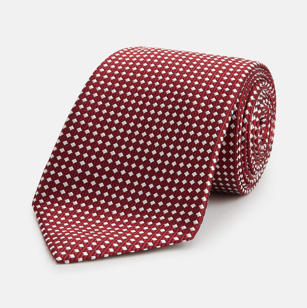 The Turnbull & Asser Slim Burgundy and White Diamond Silk Tie, shown rolled on a white background, features a repeating pattern of small white diamonds—an ideal accessory to complement any office shirt.