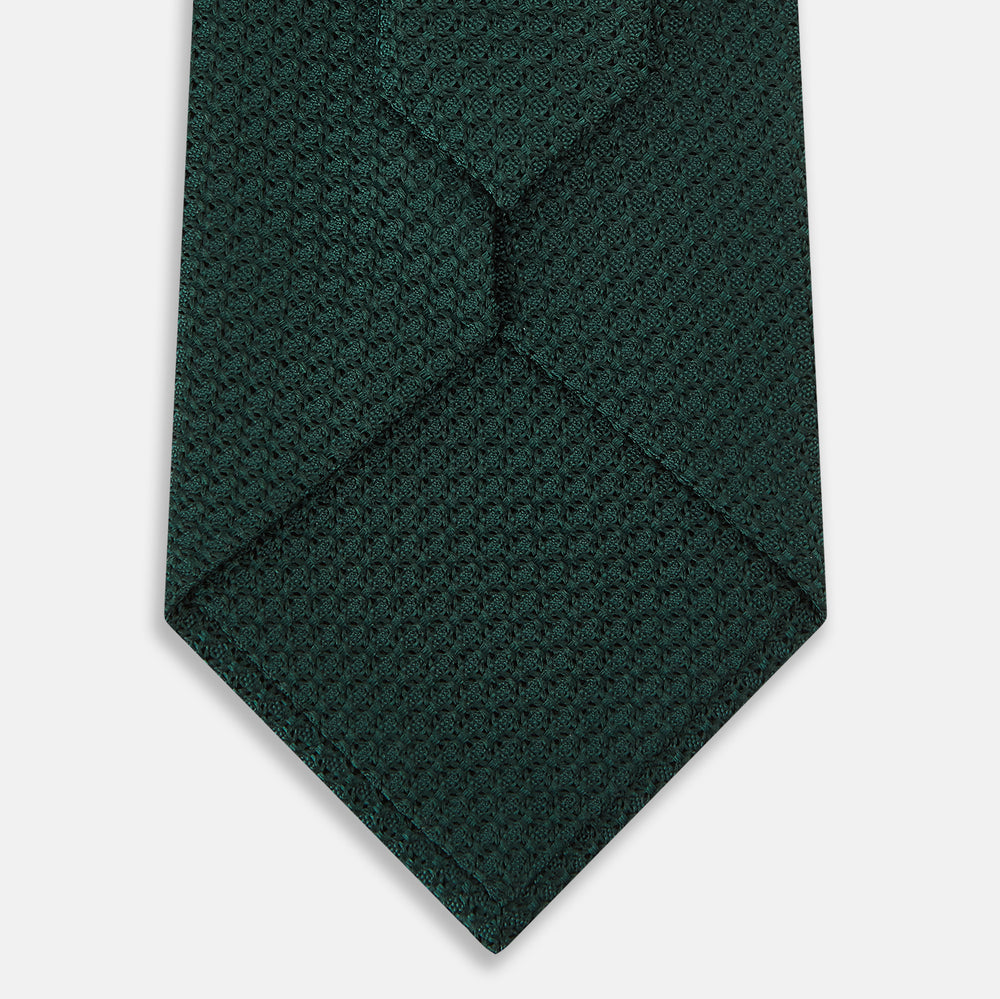 A Dark Green Grenadine Silk Tie by Turnbull & Asser UK, featuring a textured knit, is rolled up at one end and displayed on a white background.