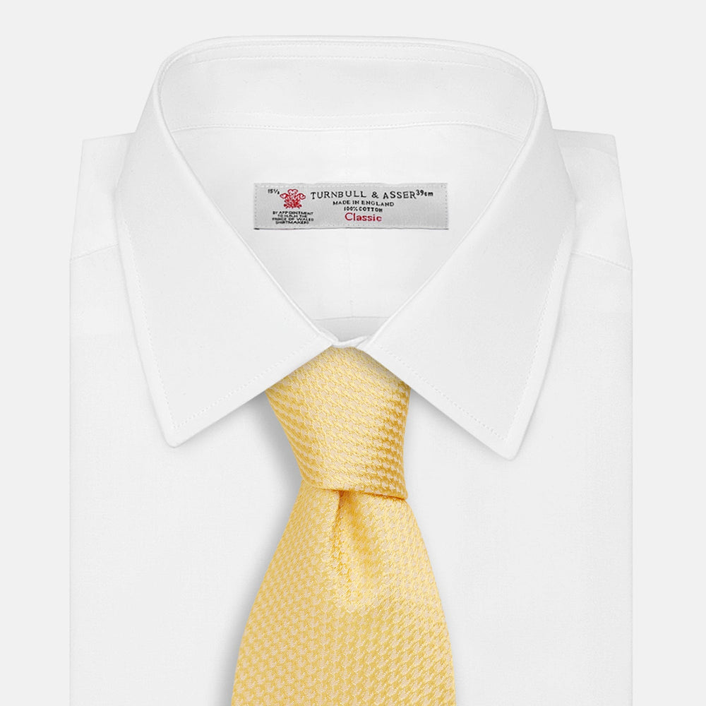 The Turnbull & Asser Yellow Lace Silk Tie, featuring a light yellow hue and subtle texture, is neatly rolled and displayed on a plain white background.