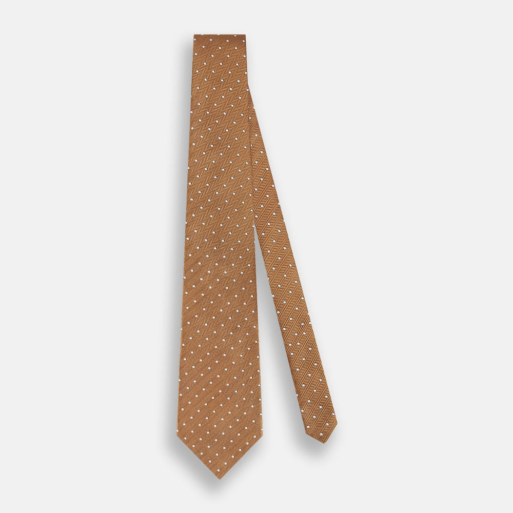 The Turnbull & Asser Camel and White Small Spot Herringbone Silk Tie features a stylish herringbone pattern with white spots—an elegant accessory ideal for modern office attire.