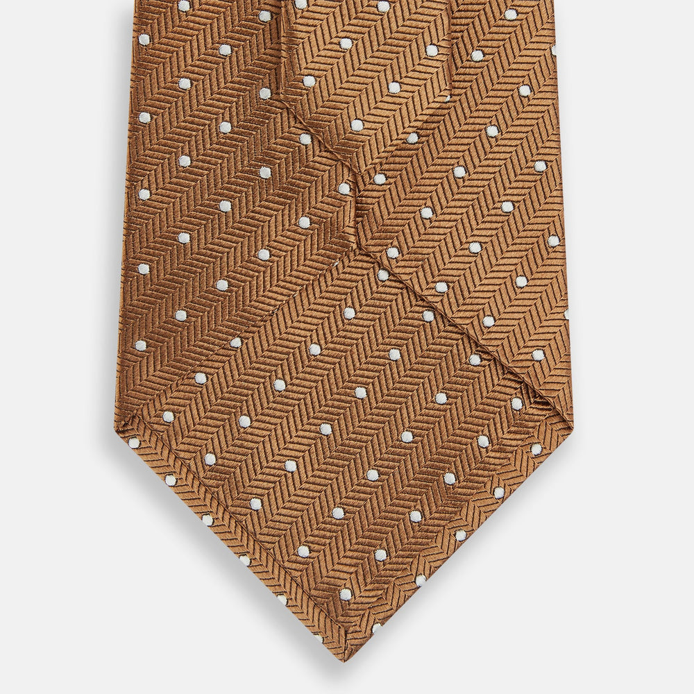 The Turnbull & Asser Camel and White Small Spot Herringbone Silk Tie features a stylish herringbone pattern with white spots—an elegant accessory ideal for modern office attire.
