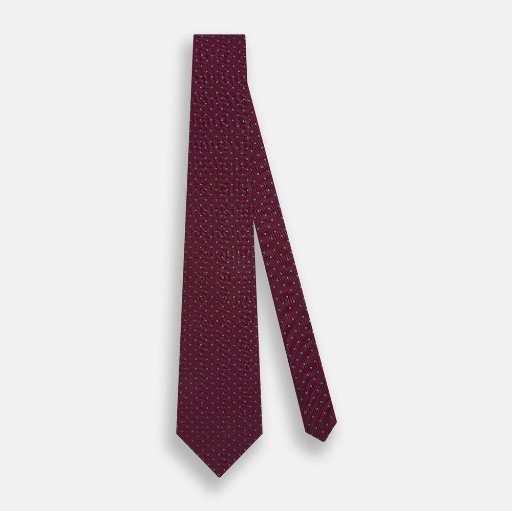 A rolled-up Turnbull & Asser Green and Magenta Micro Dot Silk Tie, featuring small, evenly spaced magenta dots on green silk, displayed on a plain white background—an ideal accessory for sophisticated outfits.