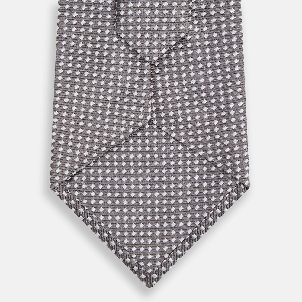 The Turnbull & Asser Grey and White Diamond Silk Tie features a refined geometric pattern, combining silver triangles on a white background for an elegant look.