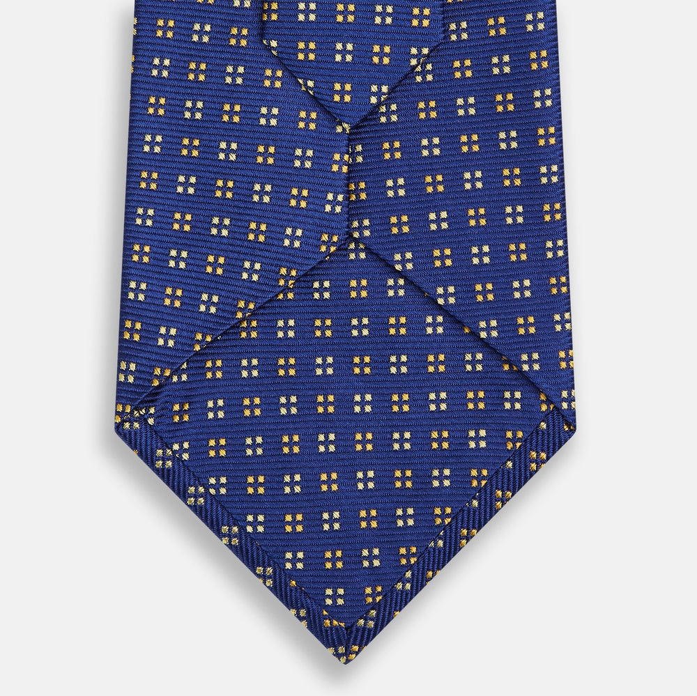 The Turnbull & Asser Blue and Yellow Multi Dot Silk Tie features a geometric yellow and white pattern, ideal for modern office wear. The elegant silk tie is showcased rolled up on a plain white background.