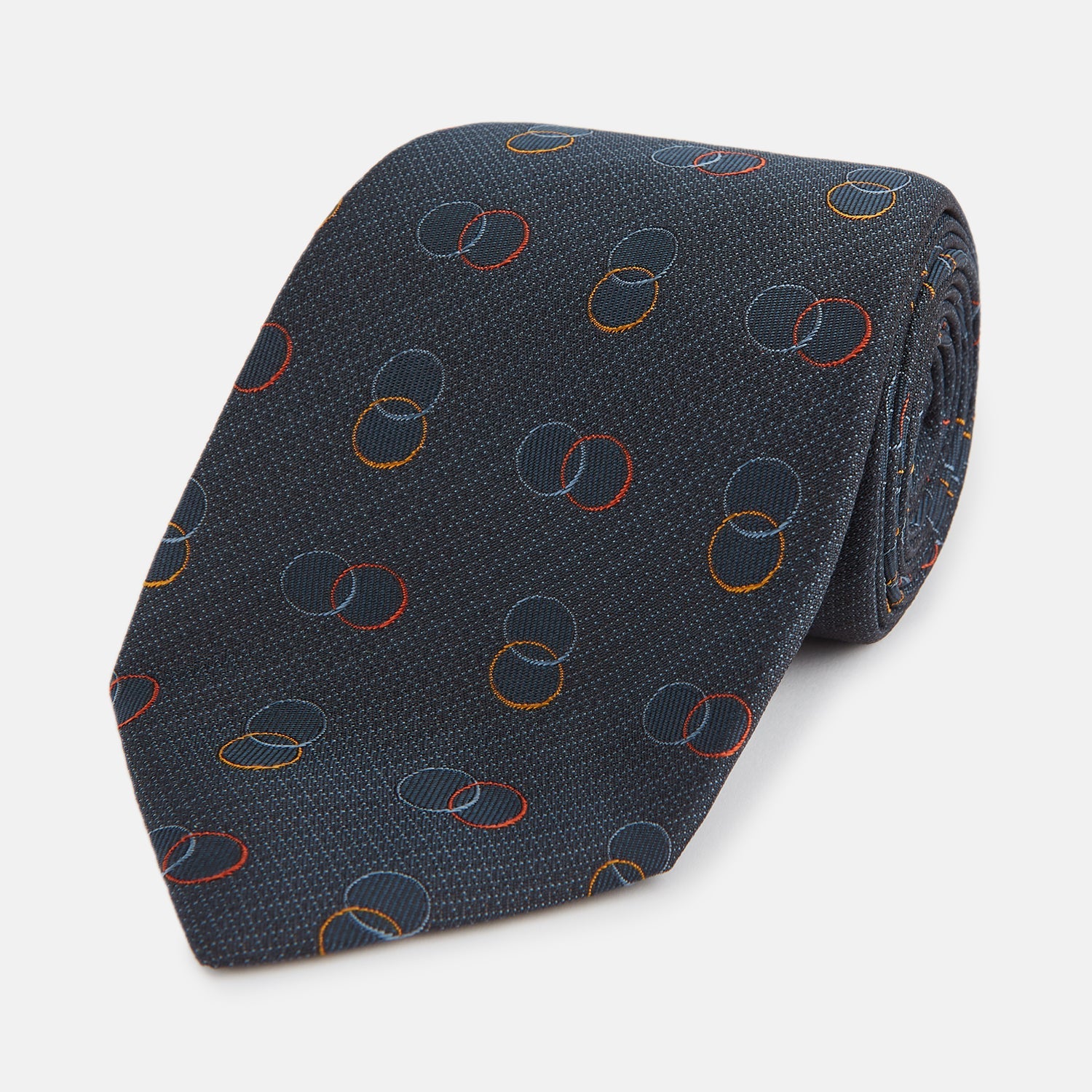 View 1 of product The Navy Links Silk Tie by Turnbull & Asser, featuring a pattern of overlapping red, yellow, and blue rings, is rolled up and displayed against a plain white background.