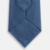 View 3 of product The Turnbull & Asser Blue Geometric Silk Tie features a textured woven pattern with lighter blue accents, shown neatly rolled on a plain white background.