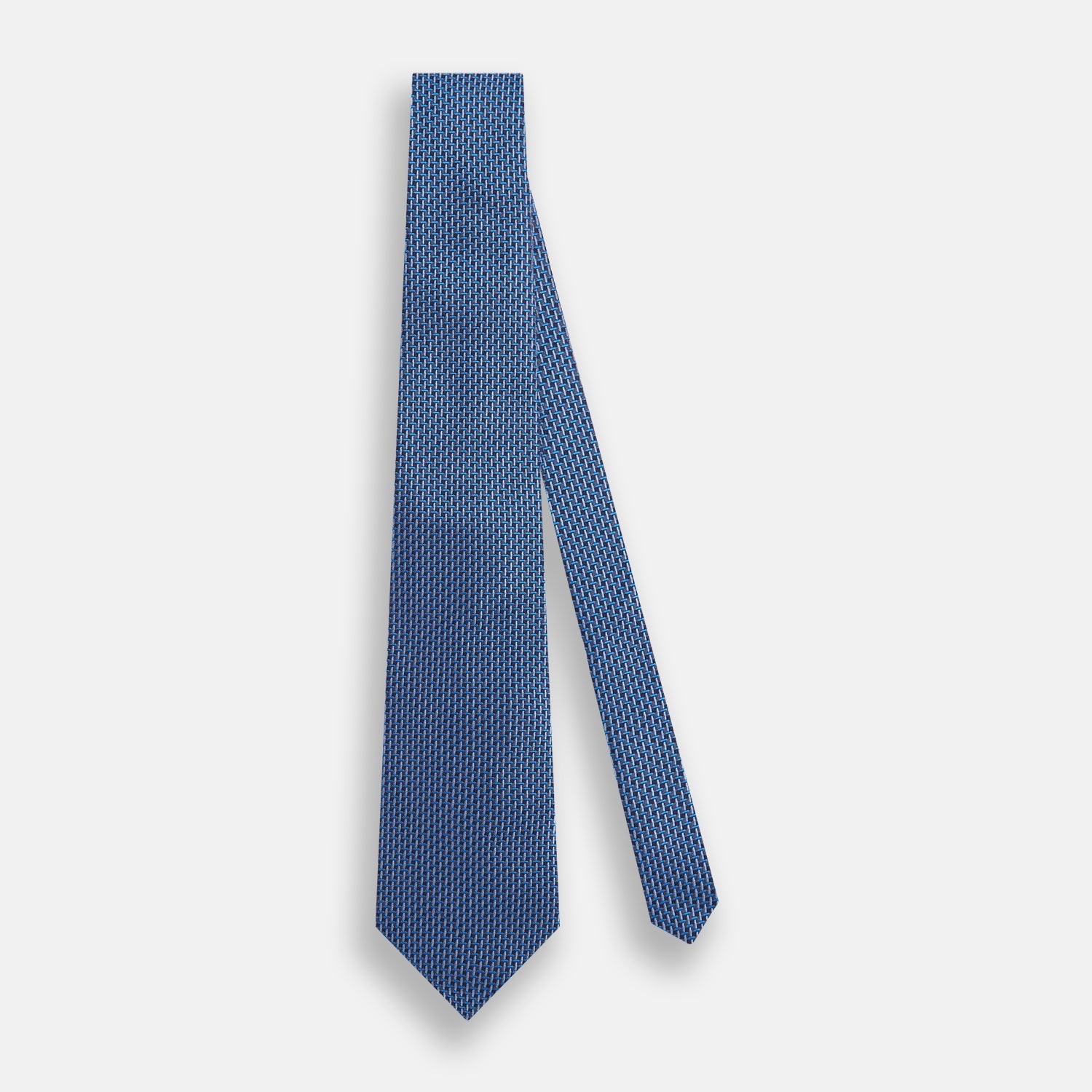 View 2 of product The Turnbull & Asser Blue Geometric Silk Tie features a textured woven pattern with lighter blue accents, shown neatly rolled on a plain white background.