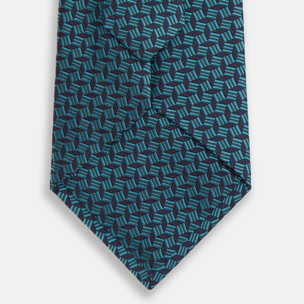 The Turnbull & Asser Turquoise Geometric Silk Tie features interlocking blue and teal cubes for a 3D effect, offering British elegance. Shown rolled up on a plain white background.