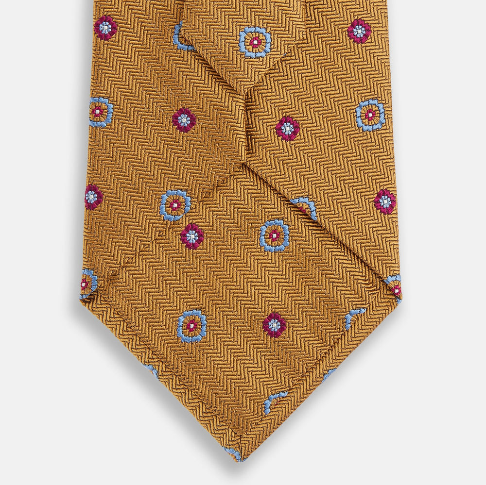 The Gold Motif Silk Tie by Turnbull & Asser features a refined yellow herringbone texture with blue and red floral accents, capturing British elegance—a sophisticated addition to any discriminating wardrobe.