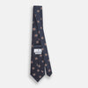 View 4 of product The Turnbull & Asser Grey Square Overlay Silk Tie features a refined chevron pattern with gray square motifs and subtle red accents, expertly handmade for formal occasions. Presented neatly rolled on a white background.