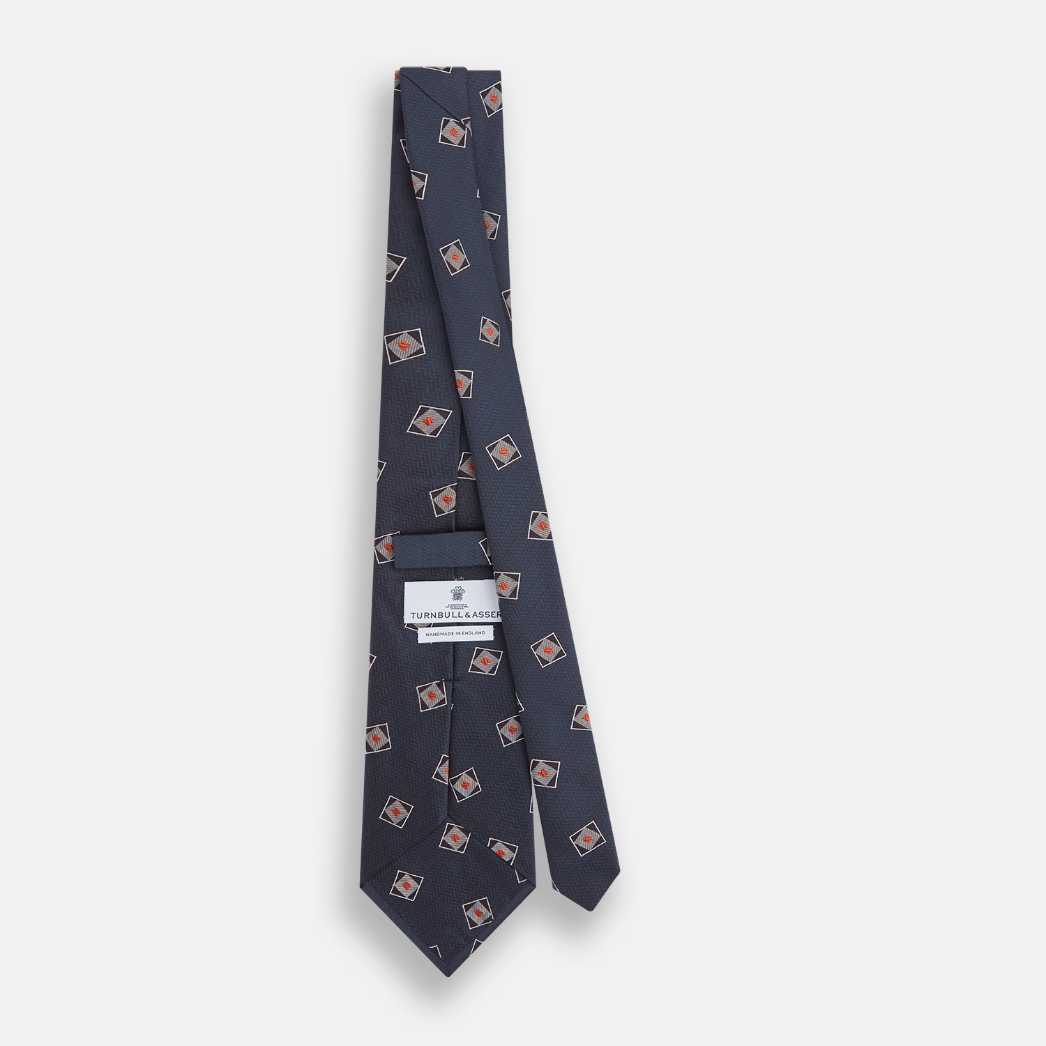 View 4 of product The Turnbull & Asser Grey Square Overlay Silk Tie features a refined chevron pattern with gray square motifs and subtle red accents, expertly handmade for formal occasions. Presented neatly rolled on a white background.