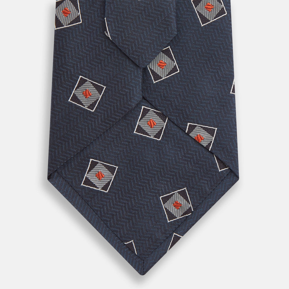 The Turnbull & Asser Grey Square Overlay Silk Tie features a refined chevron pattern with gray square motifs and subtle red accents, expertly handmade for formal occasions. Presented neatly rolled on a white background.