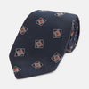 View 1 of product The Turnbull & Asser Grey Square Overlay Silk Tie features a refined chevron pattern with gray square motifs and subtle red accents, expertly handmade for formal occasions. Presented neatly rolled on a white background.