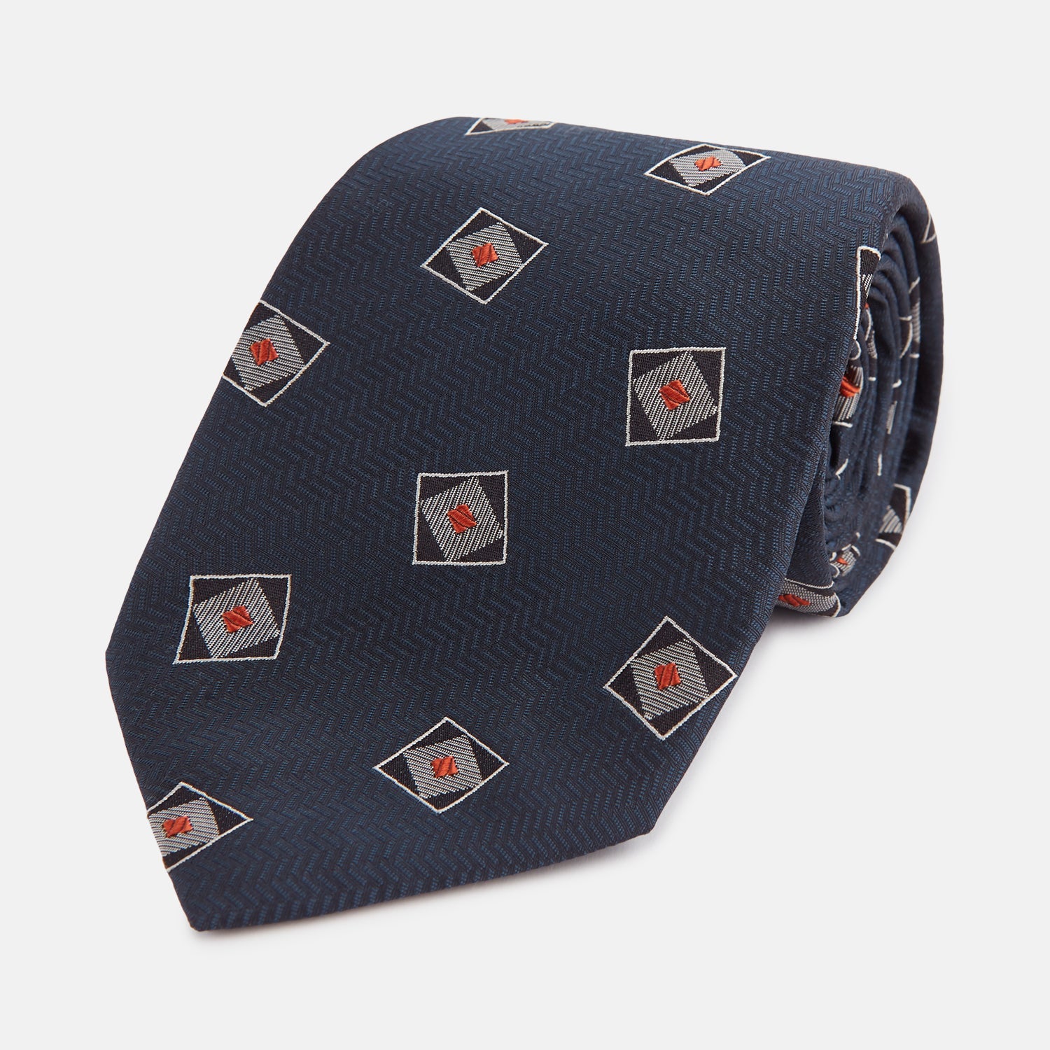 View 1 of product The Turnbull & Asser Grey Square Overlay Silk Tie features a refined chevron pattern with gray square motifs and subtle red accents, expertly handmade for formal occasions. Presented neatly rolled on a white background.