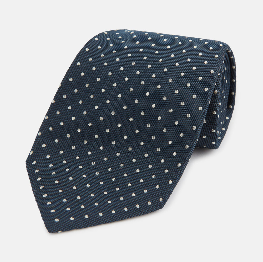 The Turnbull & Asser Navy Micro Dot Silk Tie features a handmade navy blue silk fabric with evenly spaced small white dots, rolled up on a plain white background—a timeless formal accessory for any event.