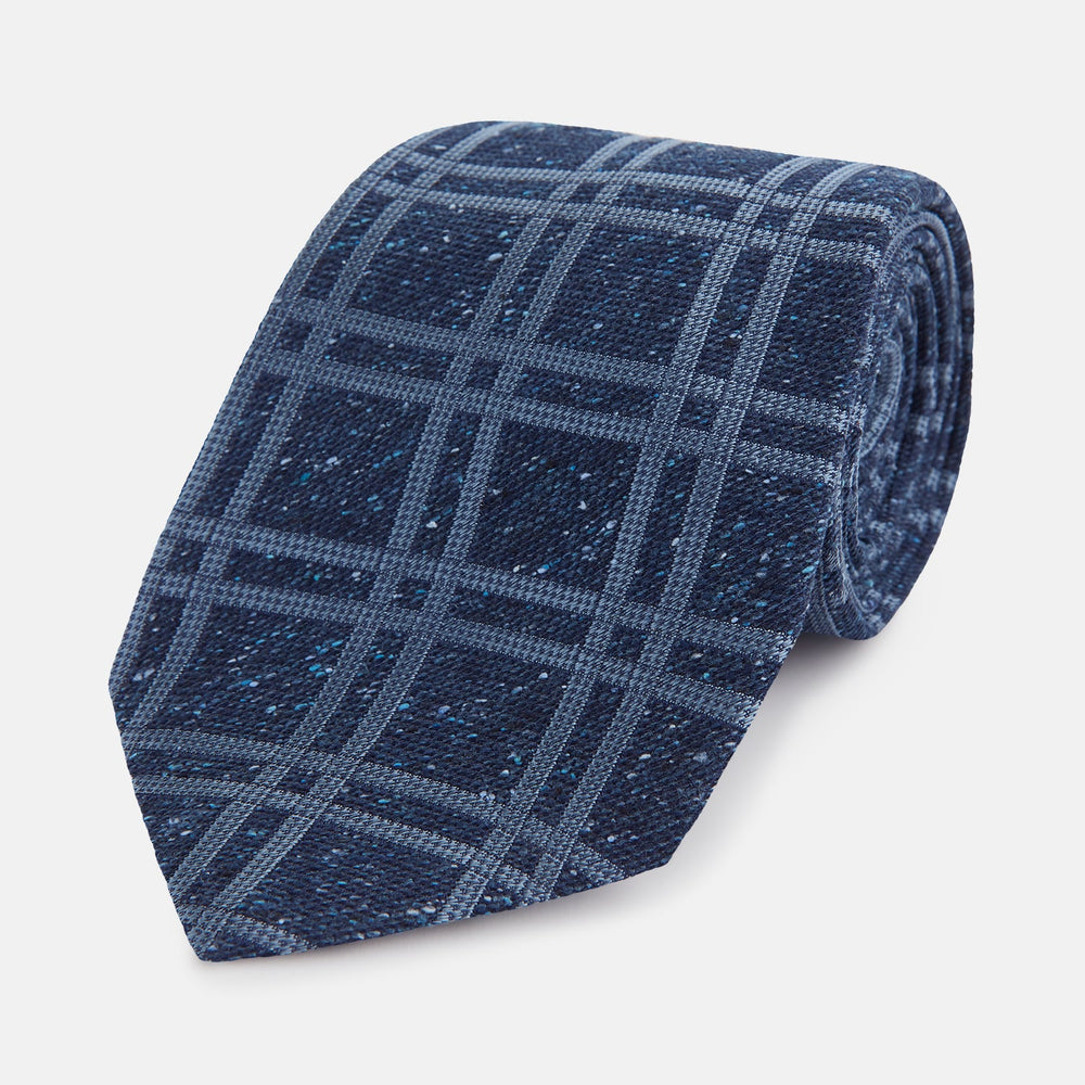 The Turnbull & Asser Navy Bold Double Check Silk Tie features a textured navy fabric with a light blue windowpane plaid pattern. This handmade silk tie is neatly rolled on a white background.