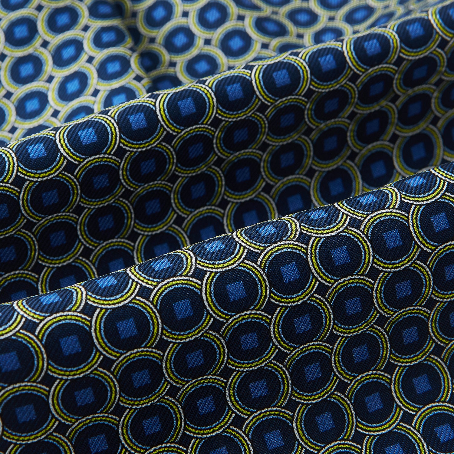View 4 of product Close-up of Turnbull & Asser UK's Navy Interlocking Circle Foulard Silk Cravat, featuring a geometric pattern of yellow and blue circles and squares. Subtle folds add texture—ideal as a refined accessory inspired by classic British style.