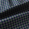 View 4 of product Close-up of the Turnbull & Asser UK Dark Navy Contrasting Rosette Medallion Printed Silk Cravat, featuring folded dark blue silk with a vibrant pattern of pink, yellow, and green rosette medallions.