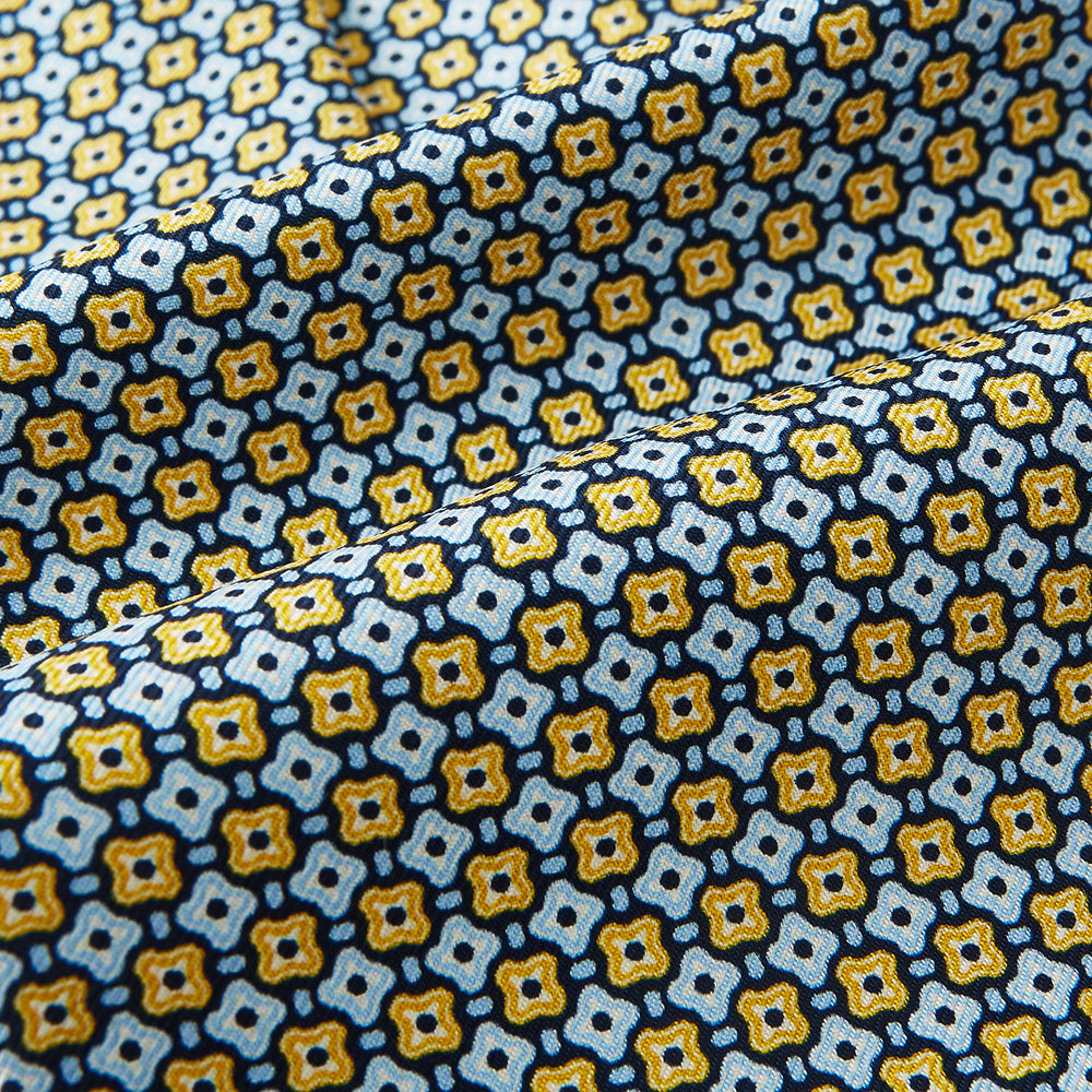 A close-up of Turnbull & Asser UK's Citrus Yellow Abstract Quatrefoil Foulard Printed Silk Cravat shows a gently folded fabric with blue, yellow, and white geometric patterns for a classic British look.