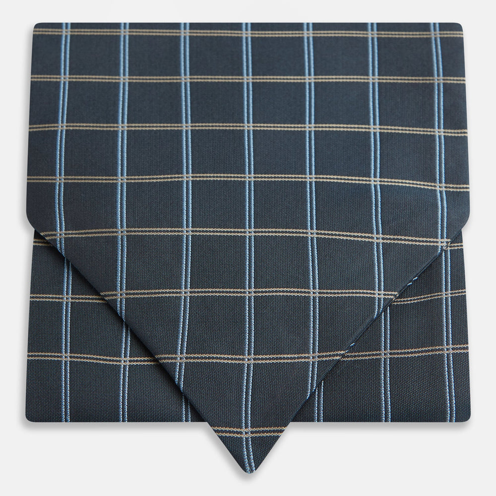 The Navy Fine Double Check Silk Cravat by Turnbull & Asser features a grid pattern in light blue and white lines—an elegant formal men's accessory, neatly folded with the pointed end at the bottom.