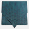View 1 of product The Turnbull & Asser Turquoise Micro Hexagon Cravat is neatly folded to show a triangular point, displayed with a matching pocket square featuring a subtle hexagon pattern, all set against a white background.
