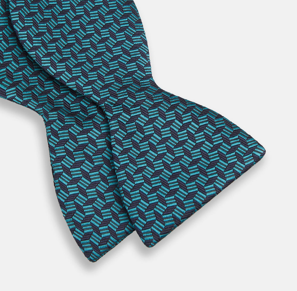 Turnbull & Asser's Turquoise Geometric Silk Bow Tie showcases British elegance with its teal and black cube pattern, set against a white background.