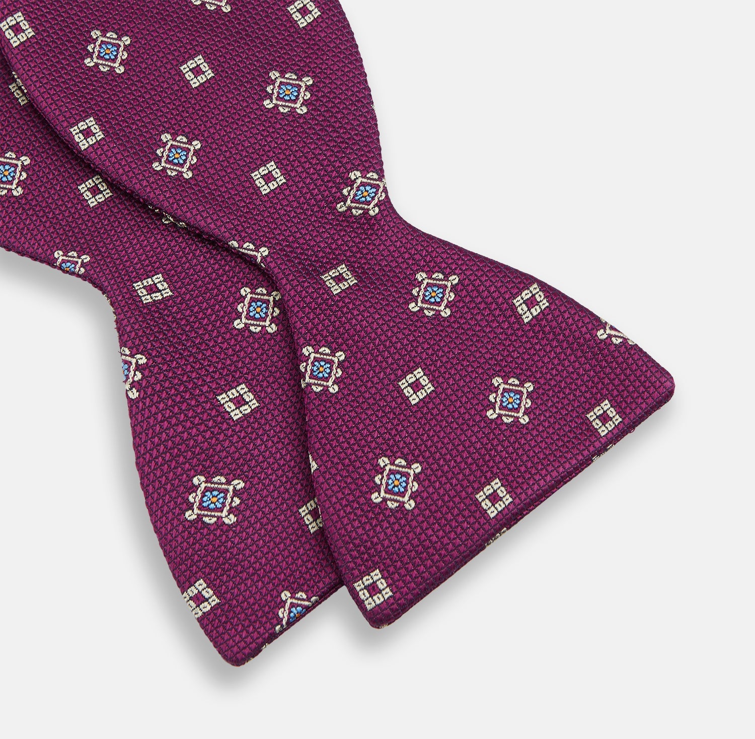 View 3 of product The Magenta Motif Silk Bow Tie by Turnbull & Asser features a textured magenta background with small, square blue, white, and gold geometric designs—an elegant choice for formal occasions.