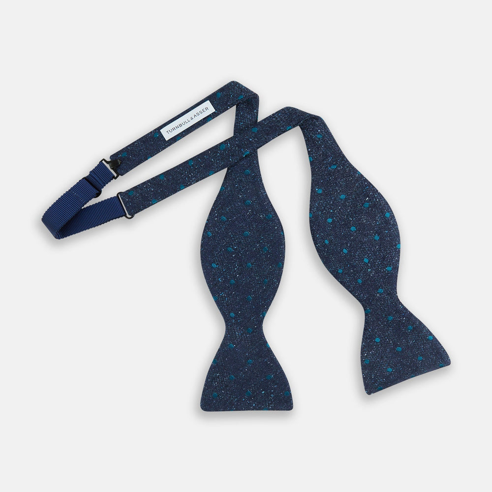 The Turnbull & Asser Teal Micro Dot Silk Bow Tie features textured navy blue silk with small teal dots, showcasing British elegance against a white background.