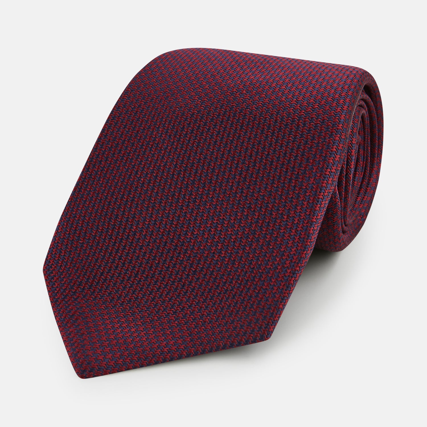 View 1 of product A close-up of the Turnbull & Asser UK Seven-Fold Navy and Red Silk Tie, featuring a small textured check pattern reminiscent of houndstooth, displayed on a plain white background.