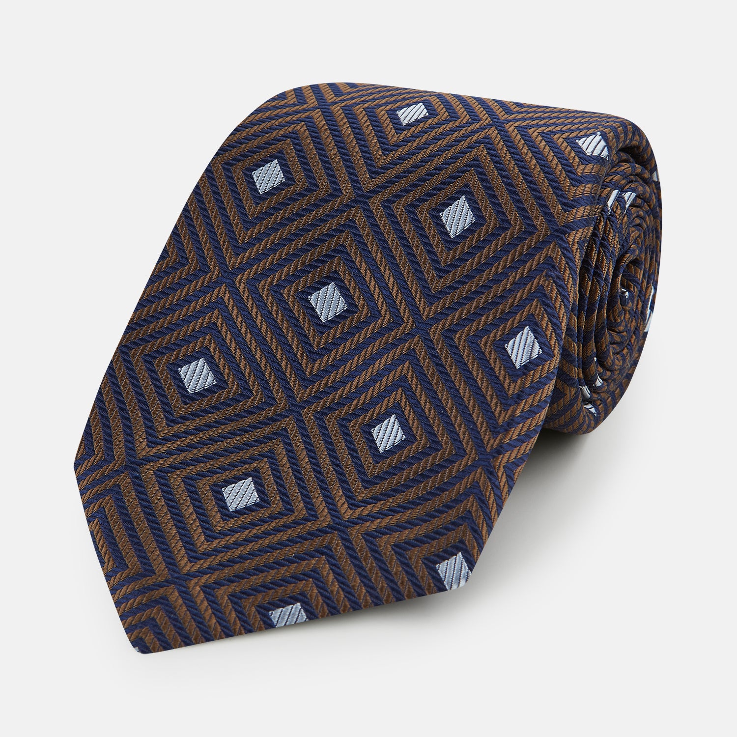 View 1 of product The Tomorrow Never Dies Seven-Fold Silk Tie by Turnbull & Asser UK features a geometric pattern of navy and brown squares with light blue diamond accents, rolled up and displayed on a plain white background.