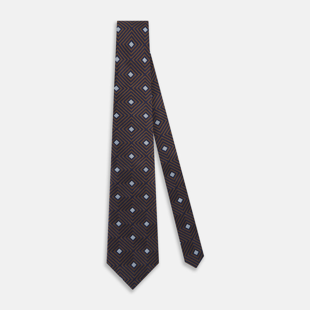 The Tomorrow Never Dies Seven-Fold Silk Tie by Turnbull & Asser UK features a geometric pattern of navy and brown squares with light blue diamond accents, rolled up and displayed on a plain white background.