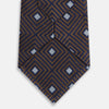 View 3 of product The Tomorrow Never Dies Seven-Fold Silk Tie by Turnbull & Asser UK features a geometric pattern of navy and brown squares with light blue diamond accents, rolled up and displayed on a plain white background.
