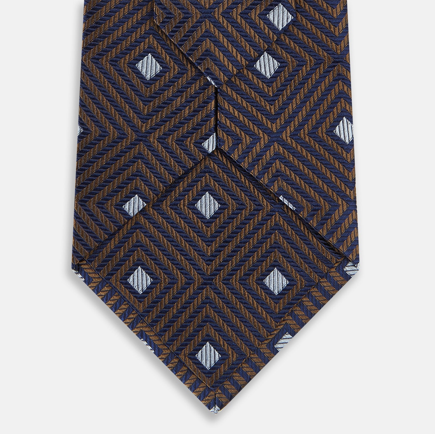 View 3 of product The Tomorrow Never Dies Seven-Fold Silk Tie by Turnbull & Asser UK features a geometric pattern of navy and brown squares with light blue diamond accents, rolled up and displayed on a plain white background.