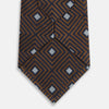 View 5 of product The Turnbull & Asser UK Tomorrow Never Dies Seven-Fold Silk Tie, as seen on James Bond, features a navy blue and brown geometric diamond pattern with silver squares at the center, set on a light background.