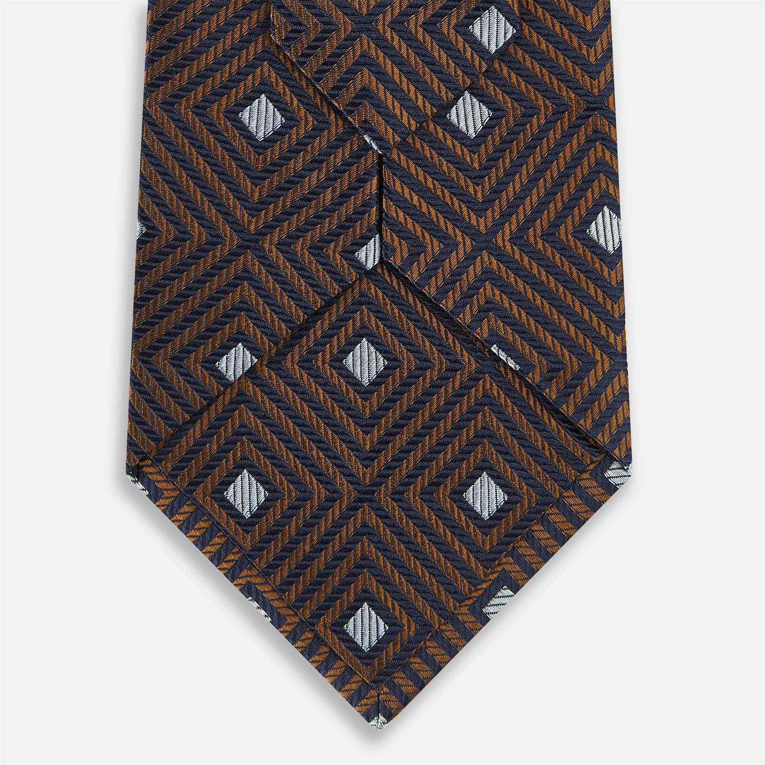 View 5 of product The Turnbull & Asser UK Tomorrow Never Dies Seven-Fold Silk Tie, as seen on James Bond, features a navy blue and brown geometric diamond pattern with silver squares at the center, set on a light background.