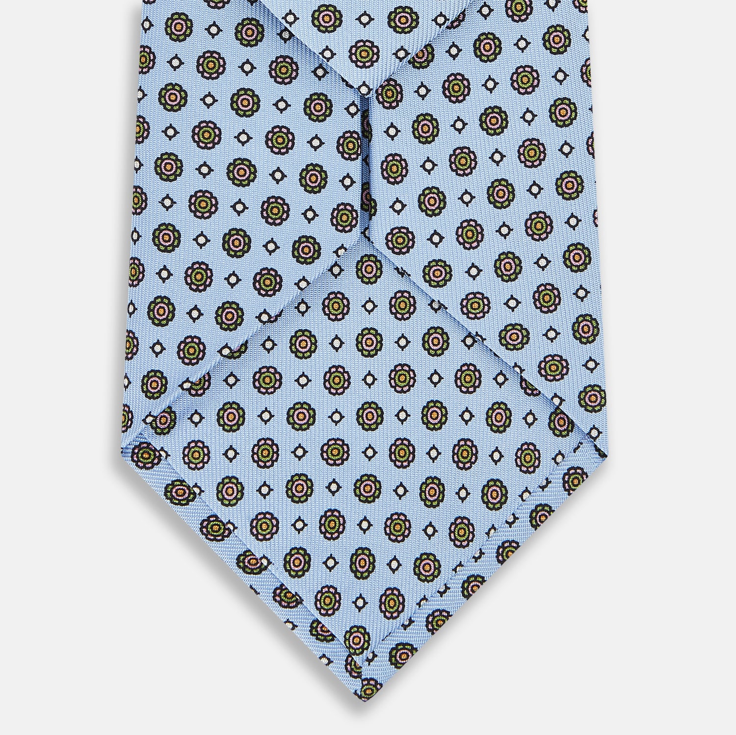 View 3 of product The Turnbull & Asser UK Great Gatsby Seven-Fold Silk Sky Tie, as seen on Jay Gatsby, is a light blue silk tie with a repeating floral medallion pattern in black, yellow, and red circles, shown rolled on a white background.