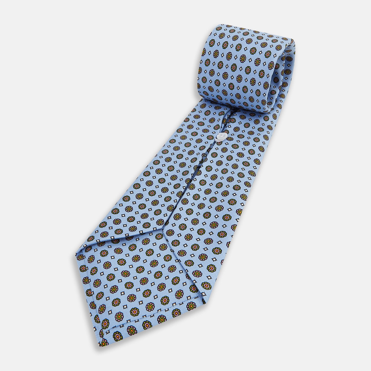View 5 of product The Turnbull & Asser UK Great Gatsby Seven-Fold Silk Sky Tie, as seen on Jay Gatsby, is a light blue silk tie with a repeating floral medallion pattern in black, yellow, and red circles, shown rolled on a white background.