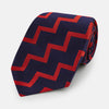 View 1 of product The Turnbull & Asser UK Seven-Fold Silk Red and Navy Geometric Tie is displayed rolled with its tip forward, showcasing its bold navy and red geometric pattern against a plain white background.