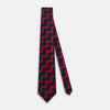 View 2 of product The Turnbull & Asser UK Seven-Fold Silk Red and Navy Geometric Tie is displayed rolled with its tip forward, showcasing its bold navy and red geometric pattern against a plain white background.