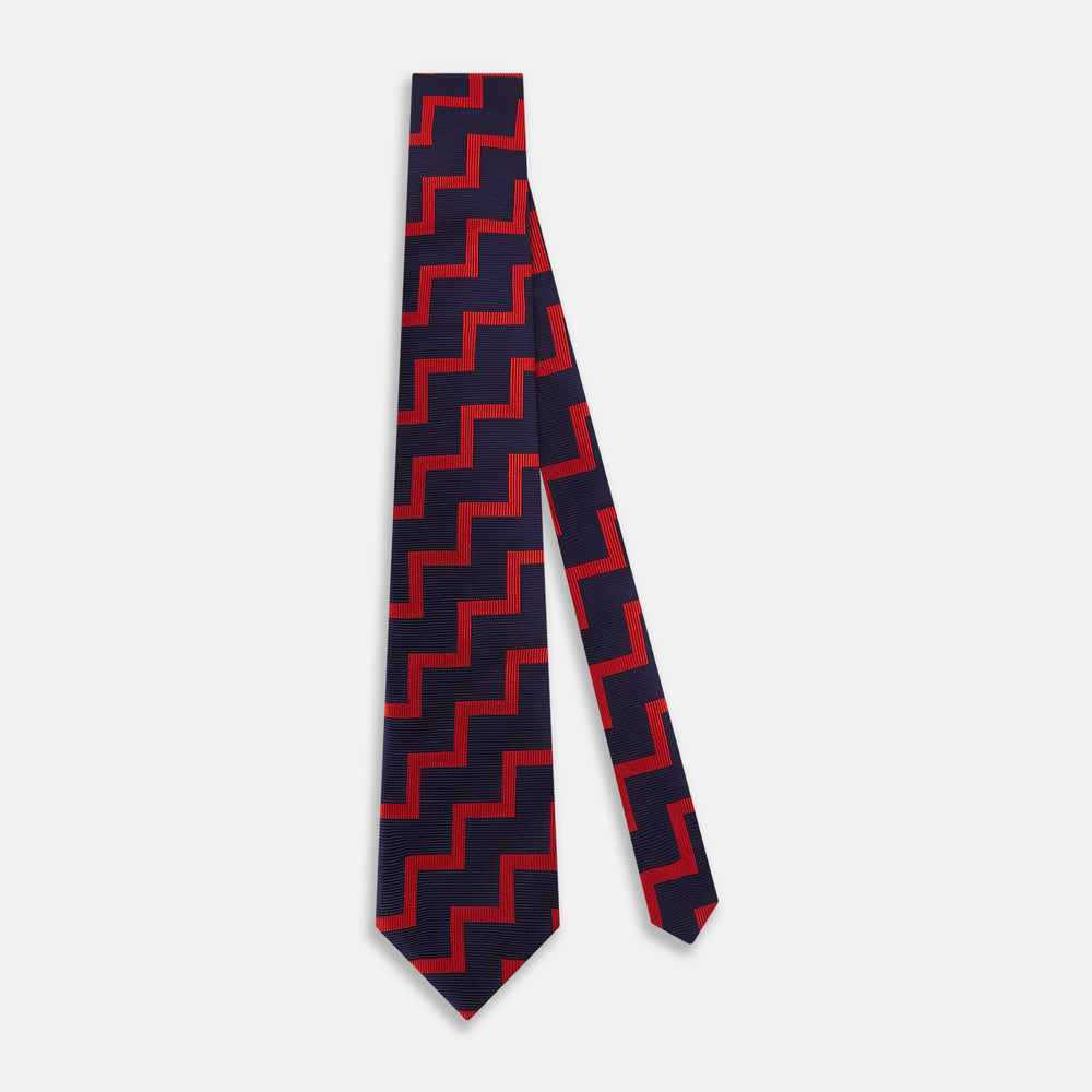 The Turnbull & Asser UK Seven-Fold Silk Red and Navy Geometric Tie is displayed rolled with its tip forward, showcasing its bold navy and red geometric pattern against a plain white background.