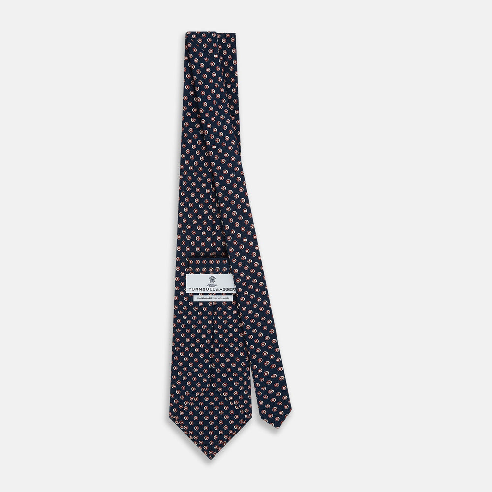 The Turnbull & Asser Navy and Red Circle Foulard Silk Tie, featuring a repeating red and white circular motif, is neatly rolled to display classic British craftsmanship.
