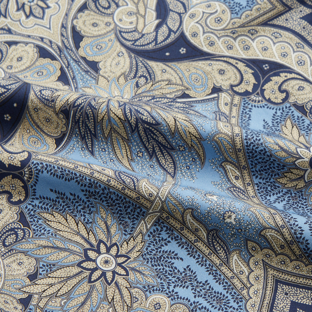 The Turnbull & Asser Pale Blue Baroque Silk-blend Hyde Pyjama Set features a long-sleeve button-up shirt and pants in a blue and beige paisley pattern, shown flat on a white background.