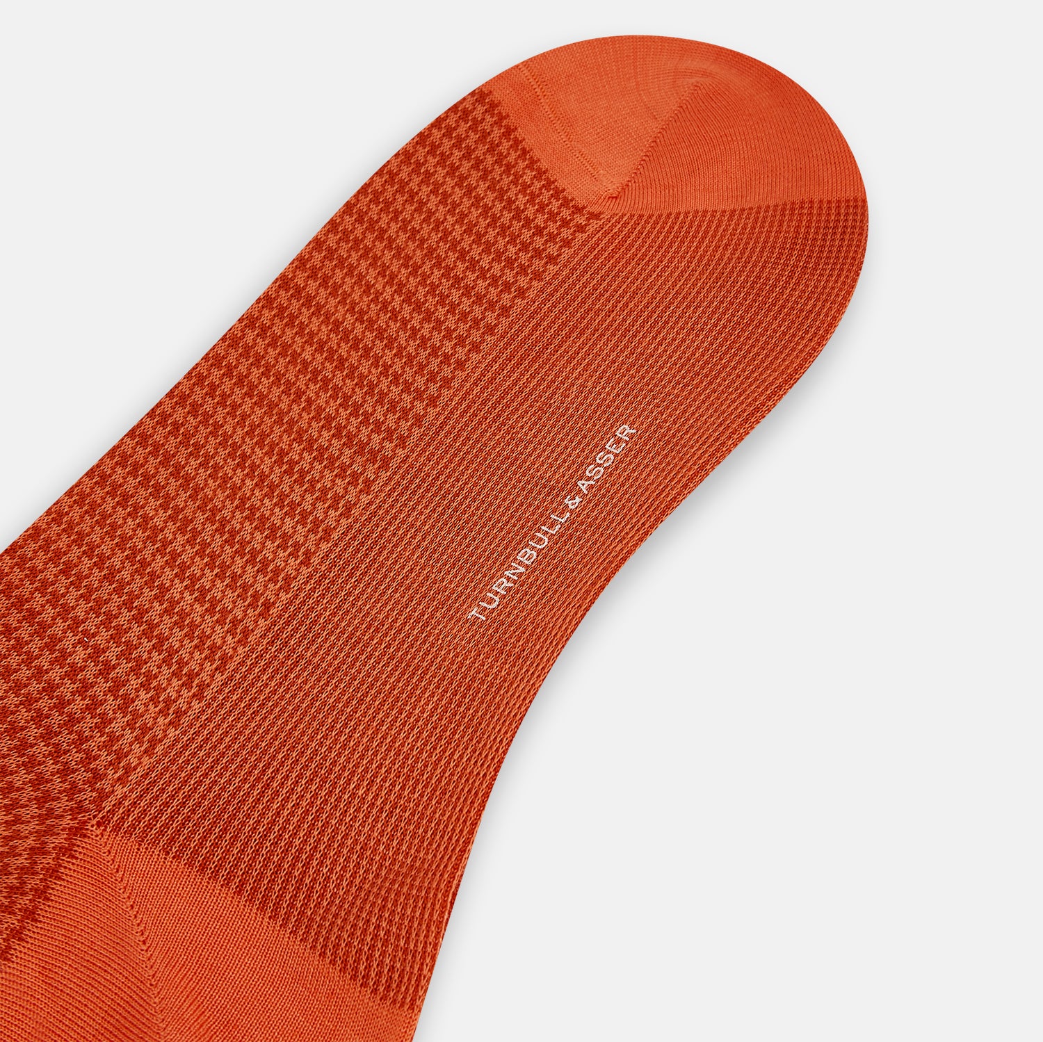 View 3 of product The Orange Houndstooth Mid-Length Socks by Turnbull & Asser feature a bold houndstooth pattern with solid orange toe, heel, and cuff, crafted from soft cotton and shown against a plain white background.