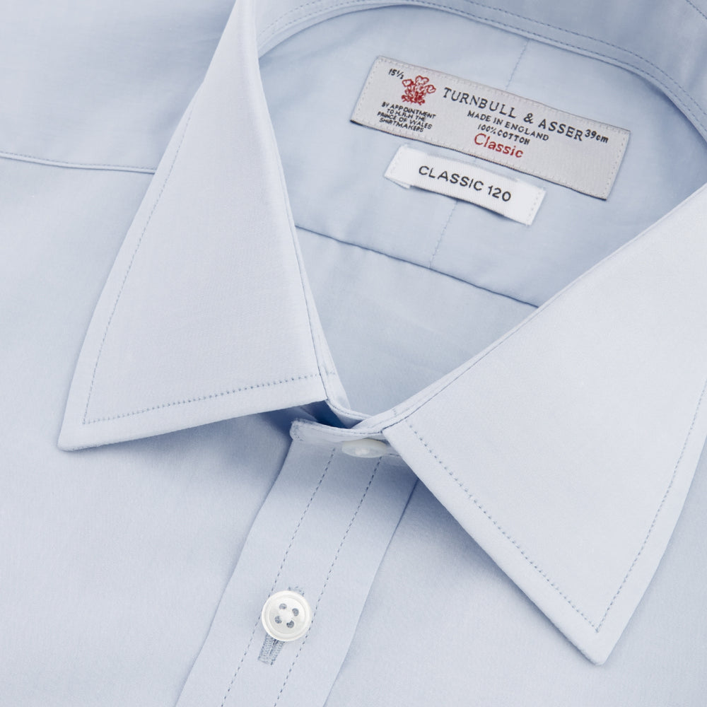The Turnbull & Asser Two-Fold 120 Light Blue Shirt features a T&A collar, 3-button cuffs, white buttons, front pocket, and inner collar label. It is displayed neatly folded on a plain white background.