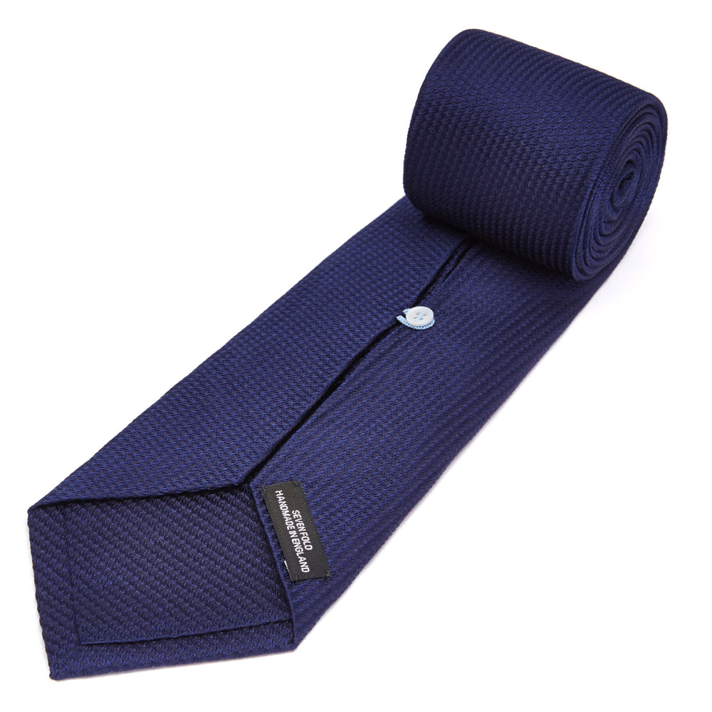 The Turnbull & Asser Seven-Fold Navy Lace Silk Tie is shown on a white background, rolled at one end with the pointed tip facing forward.