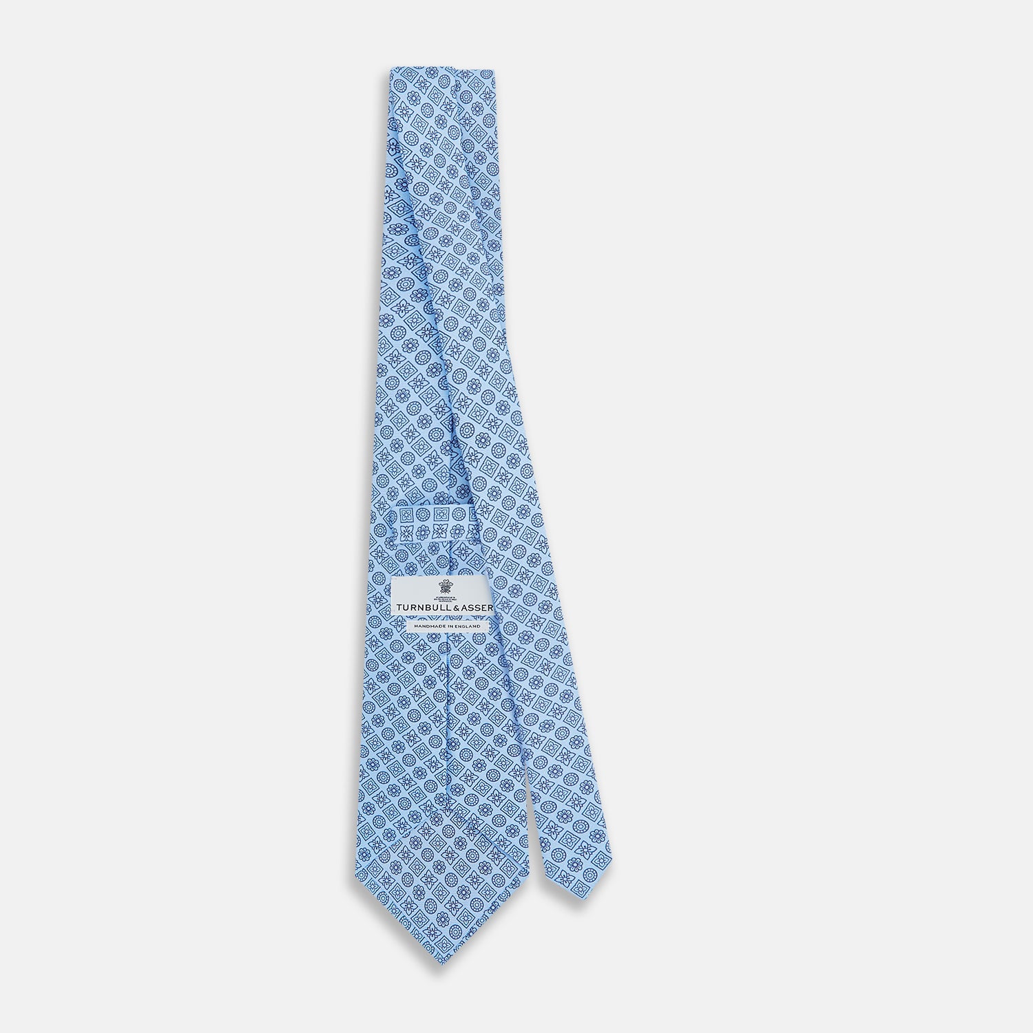 View 4 of product The Turnbull & Asser Blue Floral Tile Pattern Printed Silk Tie features a light blue geometric and floral design in dark blue, shown rolled up on a white background.