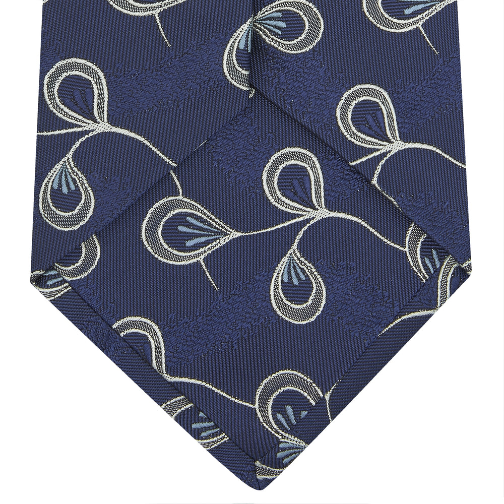 The Turnbull & Asser Navy Jacquard Silk Floral Tie features white and light blue abstract leaf designs, exemplifying fine British craftsmanship. Shown rolled up against a white background.