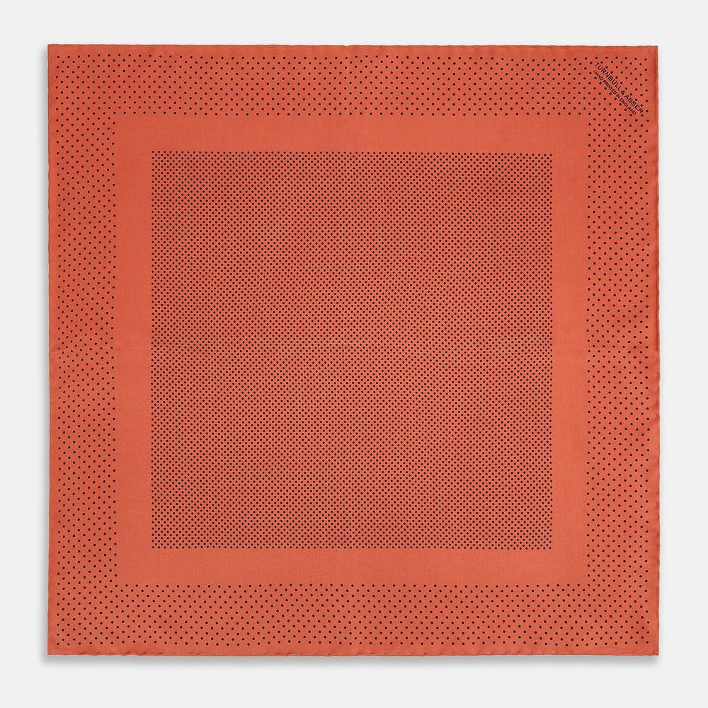 The Orange Dot Silk Pocket Square by Turnbull & Asser is handmade in England from silk, featuring small black polka dots and a solid orange border with a folded corner.