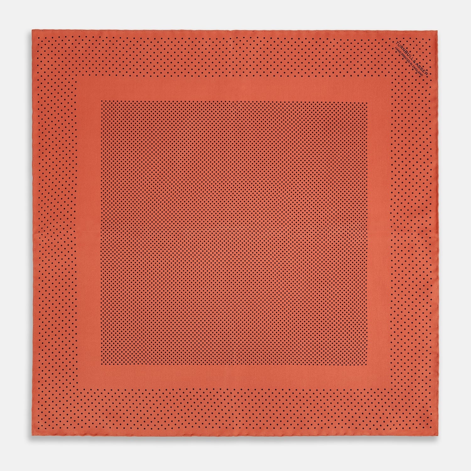 View 4 of product The Orange Dot Silk Pocket Square by Turnbull & Asser is handmade in England from silk, featuring small black polka dots and a solid orange border with a folded corner.