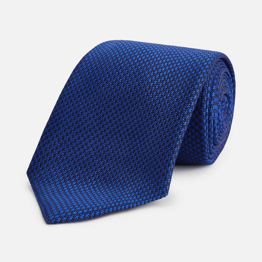 The HOUNDSTOOTH NAVY CRUISE TIE by Turnbull & Asser, featuring a textured blue design, is displayed rolled-up on a plain white background—an essential accessory for elevating formal looks.